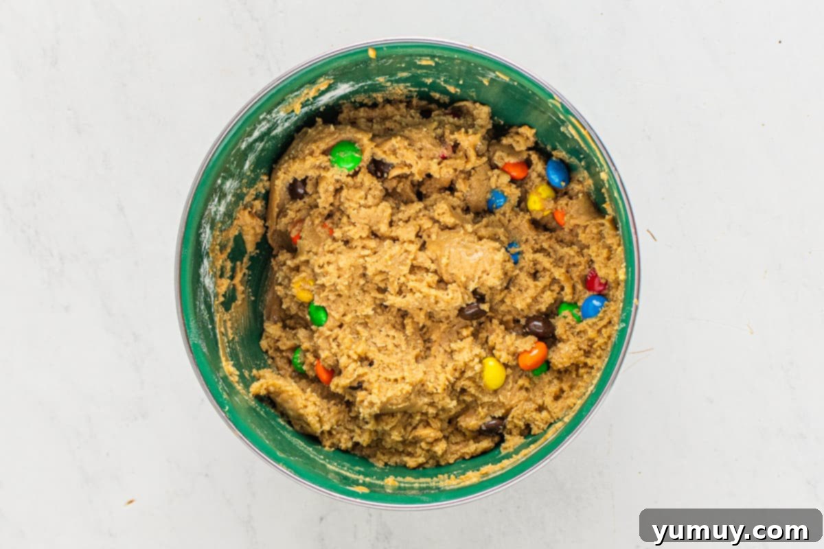 Peanut Butter M&M Blondie Bliss 6 A large mixing bowl containing wet ingredients—melted butter, oils, sugars, eggs, and vanilla—being whisked into a smooth, glossy batter.