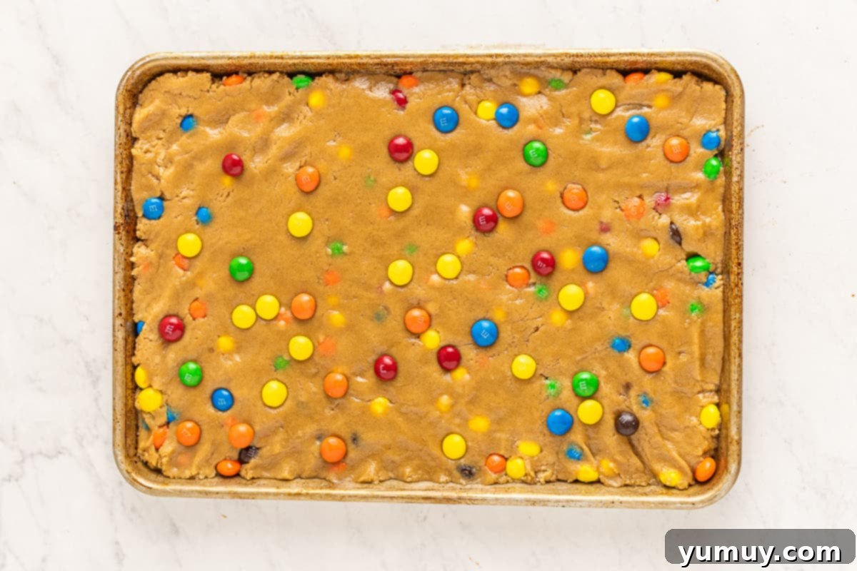 Peanut Butter M&M Blondie Bliss 7 Blondie batter with M&Ms and creamy peanut butter being folded in, creating swirls of nutty goodness.