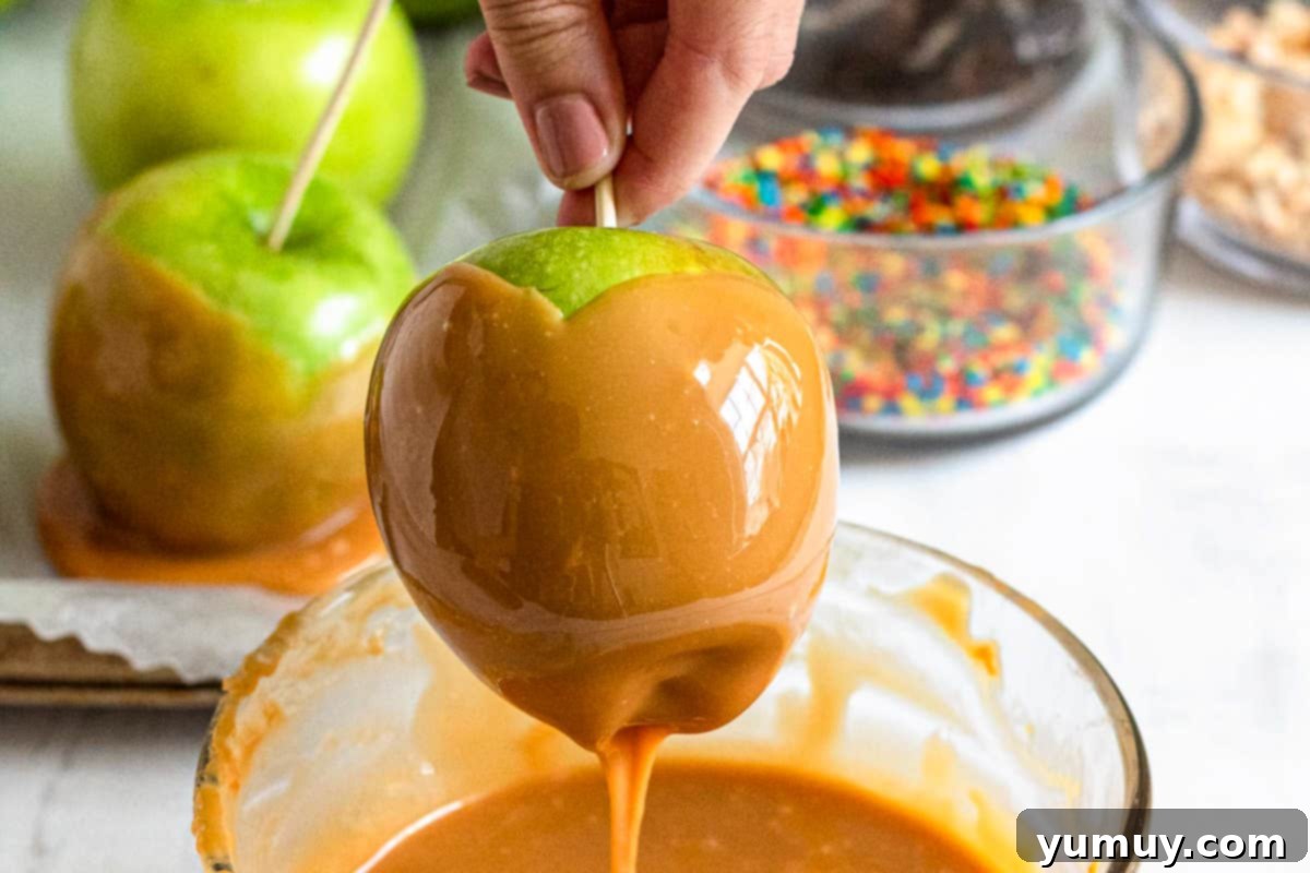 A hand dipping an apple into rich caramel, followed by rolling it in delicious toppings.