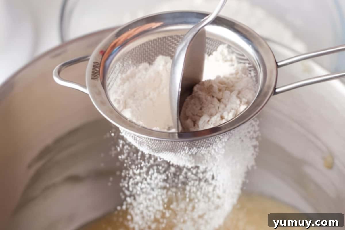 Raspberry Bliss Blondies 8 Sifting flour into creamed butter, sugar, eggs, and vanilla in a stand mixer bowl, ensuring even distribution.