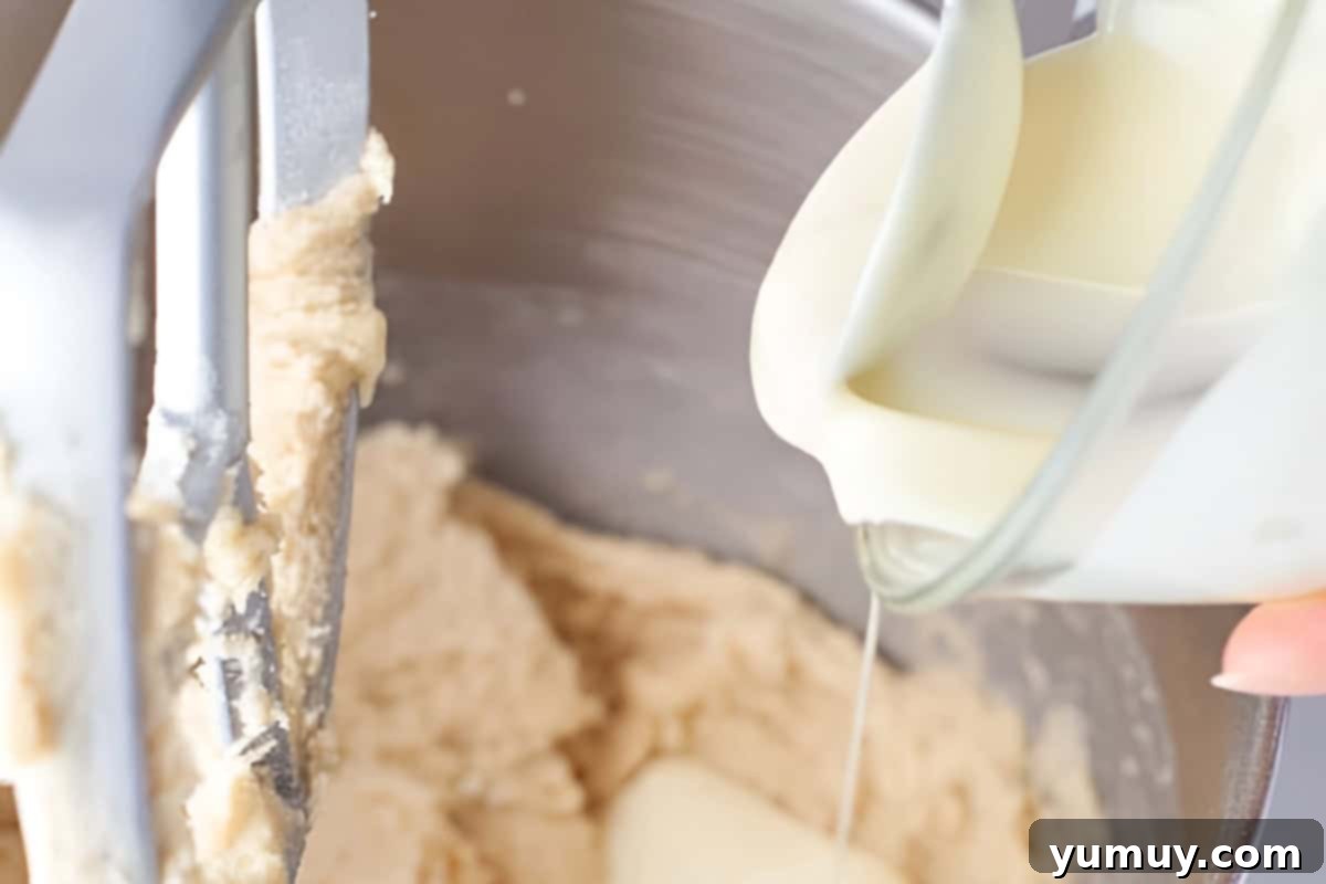 Raspberry Bliss Blondies 9 Pouring melted white chocolate into blondie batter in a stand mixer with the paddle attachment, creating a smooth and creamy mixture.